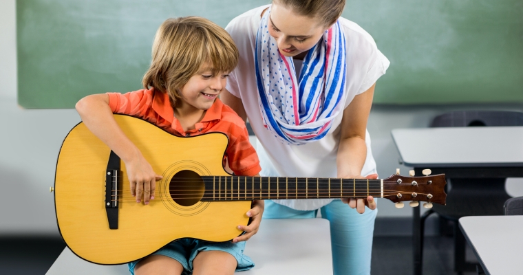 teacher assisting boy play guitar